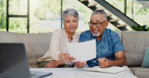 Couple de retraités examinant des documents liés à un investissement locatif autour d’une table.